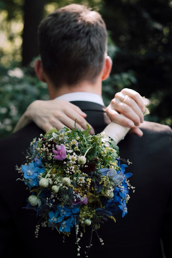 photo of the bridal bouquet with the grooms back and the bride hugging him in the background
