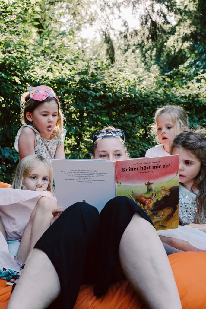 wedding guest reading children's book to a group of young girls in the garden of Teehaus Berlin in Englischer Garten